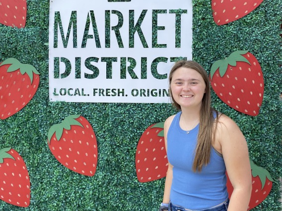 Picture of Alexis Henderson in front of a sign of the St. Jacobs Market District