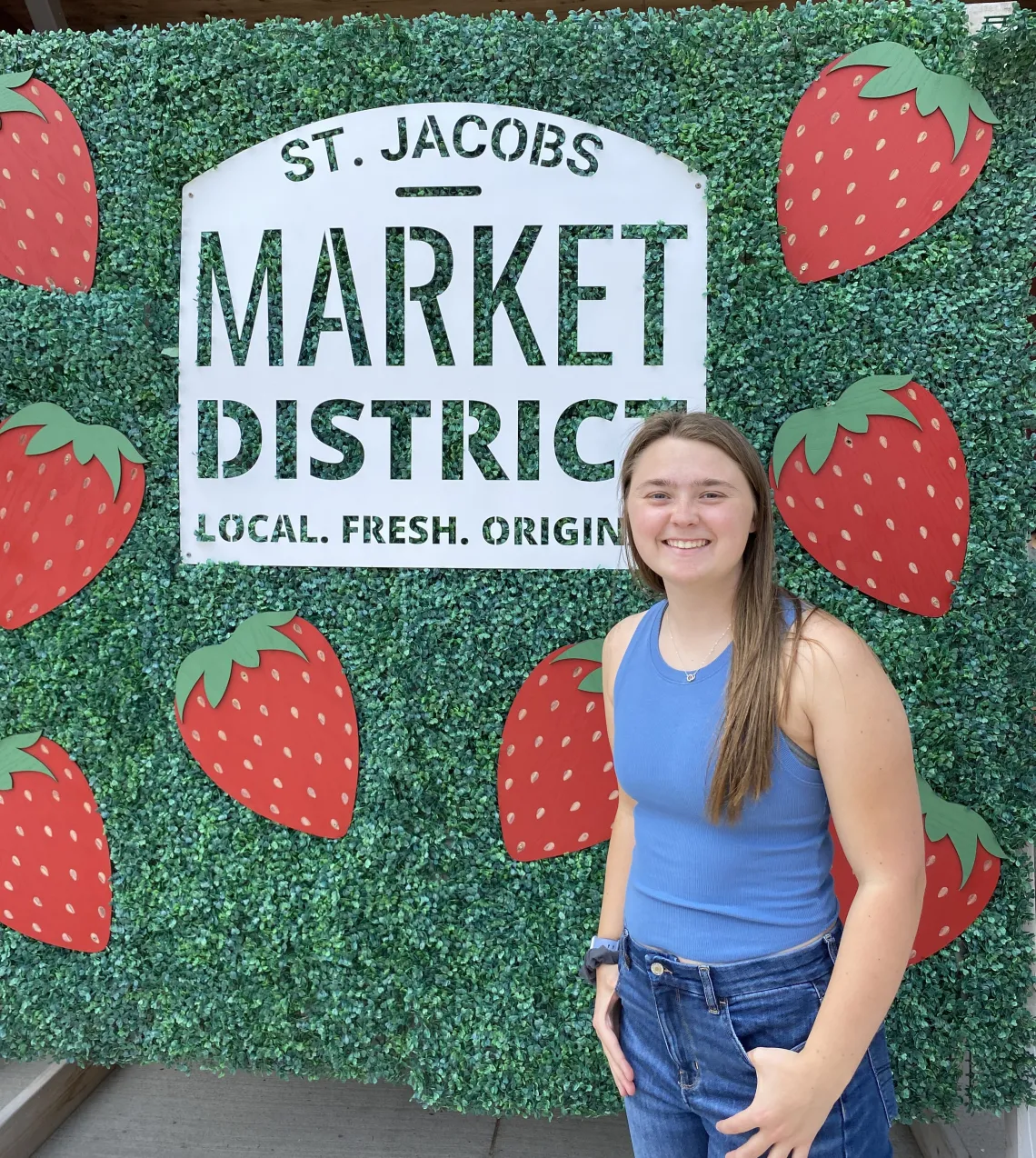 Picture of Alexis Henderson in front of a sign of the St. Jacobs Market District