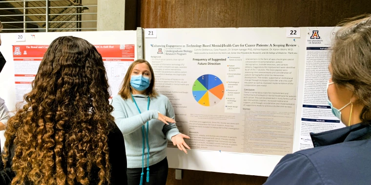 Picture of UBRP student Camille DeMarcus pointing out a figure on her poster to guests.