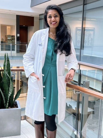 Picture of Aanika Balaji wearing a white doctor's coat, standing in a hallway